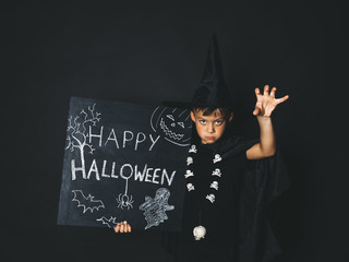 young boy dressed as a magician is holding happy halloween chalkboard in front of black background