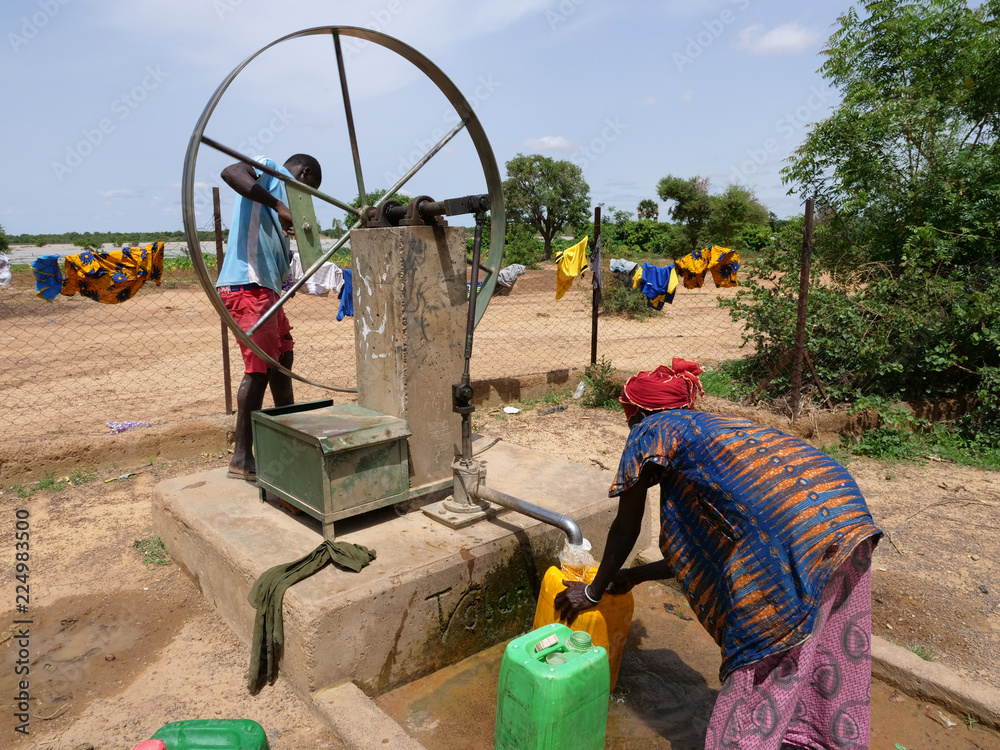 donna africana raccoglie l'acqua al pozzo  - obrazy, fototapety, plakaty 