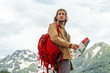 male traveler with curly hair, yellow parka and red backpack holding map and search way on mountains background