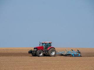 Wall Mural - Red tractor with plow on the field. Tractor on the field. Summer field and red tractor.