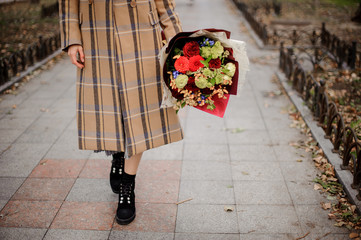 Woman in plaid coat walking with a bouquet of flowers on the alley