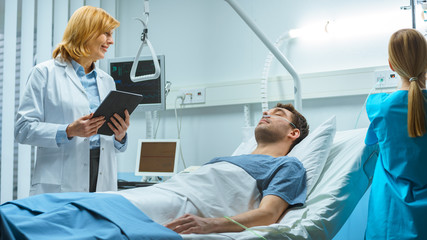 Wall Mural - Friendly Female Doctor Visits Smiling Recovering Man who is Lying in Bed, She Asks Him Questions and Fills Medical Chart, Nurse Checks His Vital Signs.