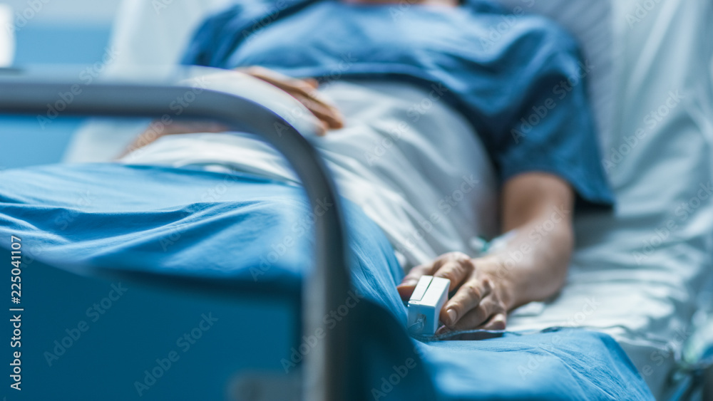 In the Hospital Sick Male Patient Sleeps on the Bed. Heart Rate Monitor Equipment is on His Finger. - obrazy, fototapety, plakaty 