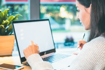 Closeup of a woman working on laptop with white screen, holding a pen