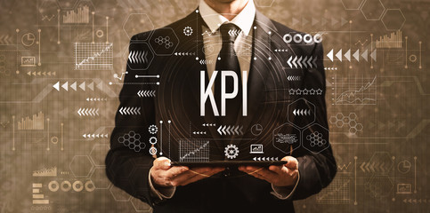 Poster - KPI with businessman holding a tablet computer on a dark vintage background
