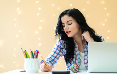 Wall Mural - Young woman with a laptop computer at a desk against an illuminated wall