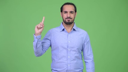 Wall Mural - Young handsome bearded Indian businessman pointing up