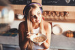 © proimagecontent - Pretty blonde long-hair girl wearing headphones sitting on the table in the red loft comfortable sunny kitchen, listening music and eating her tasty cornflakes with milk on the breakfast