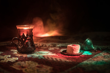 Arabian tea in glass with eastern snacks on a carpet on dark background with lights and smoke. Eastern tea concept. Empty space.