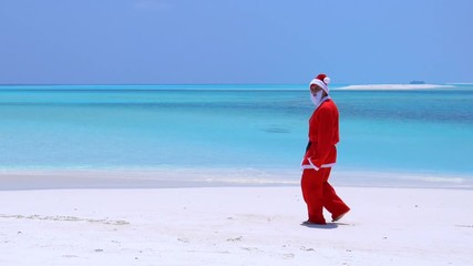 Wall Mural - Man in Santa Claus Hat walking on sandy shore