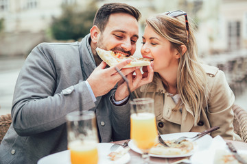 Beautiful loving couple sitting in outdoor cafe and eating pizza. Lifestyle concept