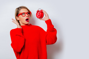 Wall Mural - Portrait of a beautiful white woman in red sweater with little alarm clock on white background, isolated.