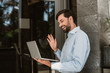 © Yakobchuk Olena - Smiling man is using notebook for video chatting outdoor. He is holding computer and waving hand to interlocutor with joy