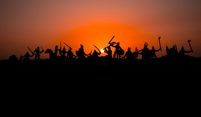 Medieval battle scene with cavalry and infantry. Silhouettes of figures as separate objects, fight between warriors on sunset foggy background.