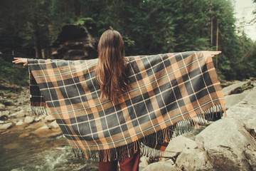 Wall Mural - Rear view of a nice young woman covered with blanked standing on the bank of the mountain river