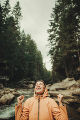 Wall Mural - Happy attractive young woman standing near mountain river while enjoying her active weekend