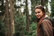 © Yakobchuk Olena - Enjoying hike. Portrait of smiling girl with backpack travelling alone. Coniferous wood on blurred background