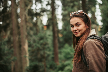 enjoying hike. portrait of smiling girl with backpack travelling alone. coniferous wood on blurred b