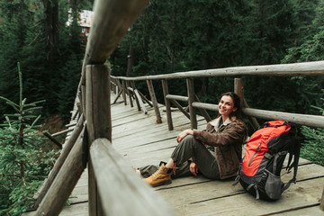 Wall Mural - Magic forest. Portrait of beautiful girl resting on bridge on the way to the camp. She is looking at camera with happy smile