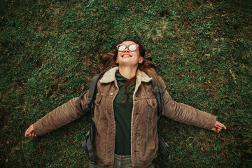 Wall Mural - I am happy and free. Top view portrait of beautiful girl in sunglasses resting on the grass. She is looking up and smiling