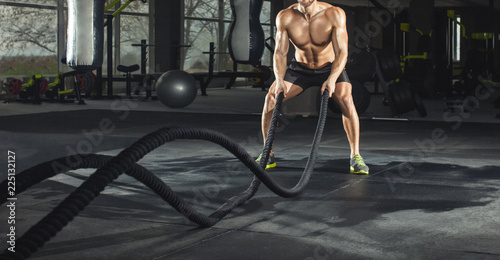 Fotografía Athletic adult man with battle rope doing exercise in the fitness gym