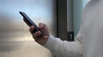 4K. Businessman using his smartphone. Person typing on the phone, surfing the internet and checking social networks. He is near an elevator-Adrian