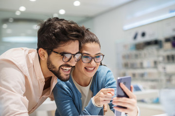 Beautiful smiling couple testing some telephones in electronic store. Smiling at looking at telephone in bright store.