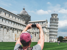 Stylish Guy With A Phone Taking Pictures Of The Leaning Tower Of Pisa On A Sunny, Clear Day. Concept Of Recreation, Travel And Tourism