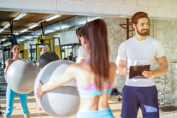 Poster - Picture of personal fitness trainer talking with his female client while she is holding big ball in her hands.