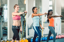 Full Length Of Three Fit And Beautiful Women Standing Up While Exercising With Fitness Resistance Bands During Workout Class For Ladies At The Gym