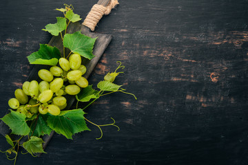 Fresh green grapes with leaves of grapes. Top view. On a black wooden background. Free space for text.