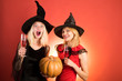 © Volodymyr - Portrait of two happy young women in black witch halloween costumes on party over orange background. Beautiful young surprised woman in witches hat and costume holding pumpkin.