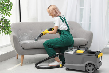 Canvas Print - Female janitor removing dirt from sofa with upholstery cleaner in room