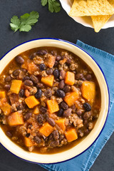 Wall Mural - Homemade chili con carne with mincemeat, red and black beans, tomato sauce and pumpkin with tortilla chips on the side, photographed overhead on slate (Selective Focus on the chili)