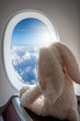 Reisen mit Kindern Konzept: Stoffhase schaut aus einem Flugzeugfenster hoch über den Wolken