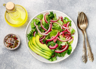 Wall Mural - Delicious vegetarian light salad of lettuce, radicchio, red onion and avocado with spices in a white plate on a concrete surface. French cuisine