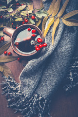 Wall Mural - Autumn concept. Gray scarf and cup of autumn berries tea decorated with fall leaves on dark rustic wooden table background , top view, still life