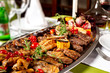 Metal dish with grilled meat set of beef tongue, pork, chicken, sausages and vegetables at decorated table background.