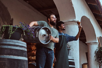 Wall Mural - Two brewers in apron standing outdoors checking the quality of brewed drink at brewery factory.