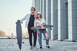 Attractive young couple dressed in trendy clothes posing with skateboards near skyscraper.