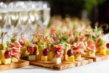 The Buffet At The Reception. Glasses Of Wine And Champagne. Assortment Of Canapes On Wooden Board. Banquet Service. Catering Food, Snacks With Cheese, Jamon, Prosciutto And Fruit