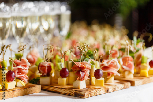 the buffet at the reception. Glasses of wine and champagne. Assortment of canapes on wooden board. Banquet service. catering food, snacks with cheese, jamon, prosciutto and fruit © malkovkosta