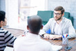 © Seventyfour - Professional recruiters sitting at table and asking question to young specialist while interviewing him in loft office