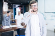 © Seventyfour - Optimistic handsome young bearded sales manager in glasses standing in board room and calling customer on mobile phone while looking at camera