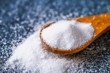 Crystals of shallow salt in a scoop, spoon on a dark gray table.