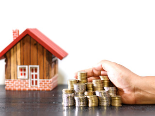 hand holding coins stack and wooden house background on desk, estate investment and financial concept