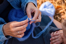 Concept Of A Freelancer Work In The Open Air. Close Up  Of A Young Woman In A Denim Jacket Knitting Blue Hat With Needle On Plaid.