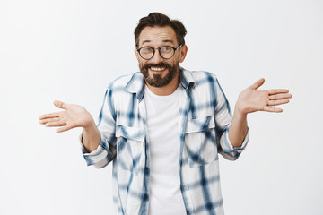 Wall Mural - Husband hid wifes phone, making innocent expression as if he unaware and clueless. Charming happy and carefree man with beard and wrinkles in glasses, shoulder shrugging with spread palms and smile