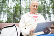 © pressmaster - Active senior man with touchpad networking while sitting on bench in park and having rest