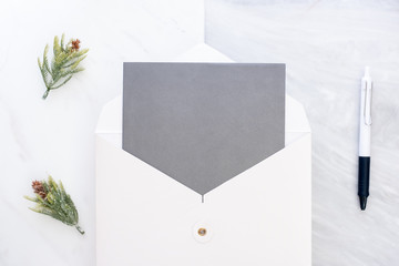 Poster - Top view of blank grey card in white envelop with pen and pine leaf on two layer step of marble table top.Mock up template for display of design.modern business items.